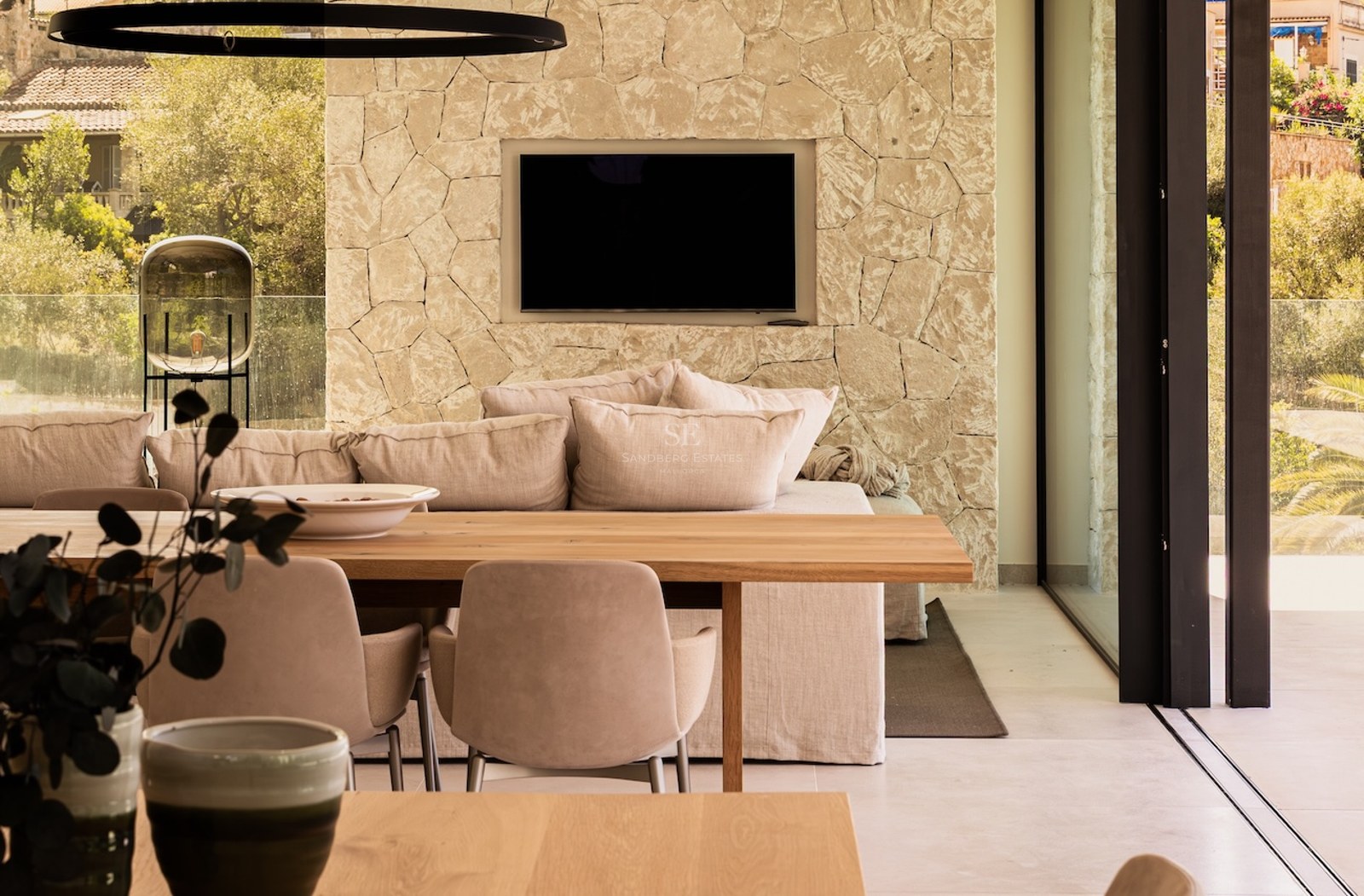 Modern living room with a stone feature wall, recessed TV, plush beige sofa, and a wooden dining table in the foreground.