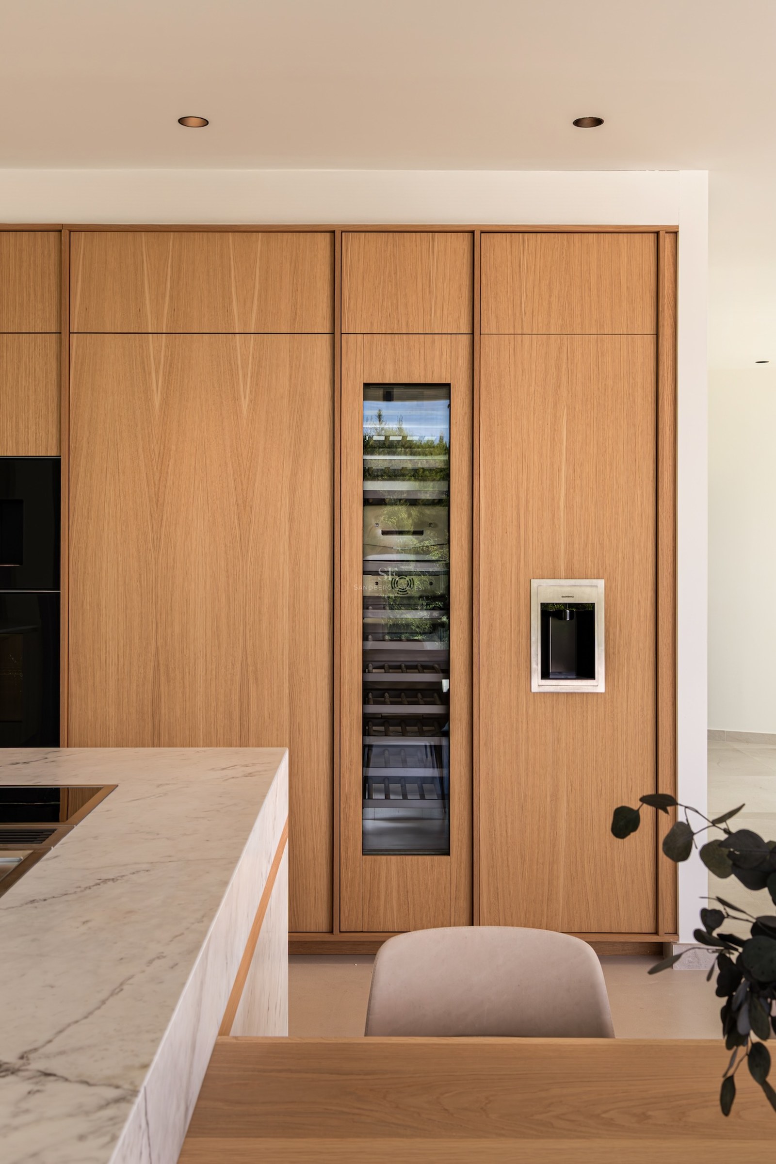 A luxury kitchen with floor-to-ceiling oak cabinetry, an integrated glass-door wine cooler, and a marble island.