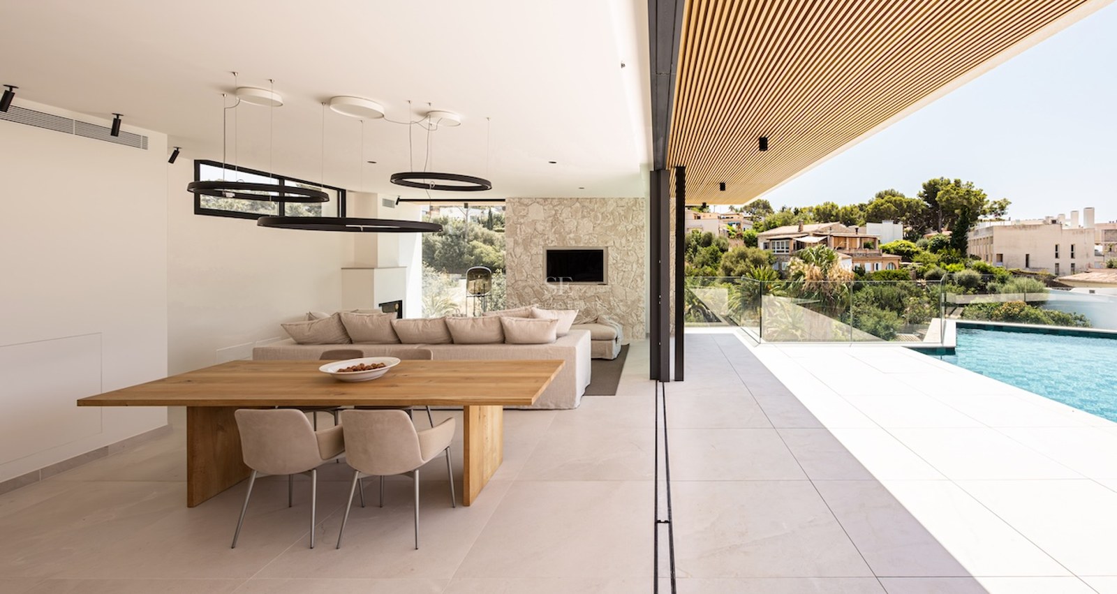 A luxury open-plan living and dining room with glass walls opening onto a terrace and infinity pool.