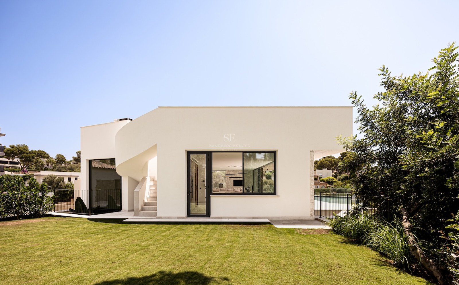 Villa blanche moderne avec escalier extérieur courbé et pelouse verdoyante sous un ciel bleu.
