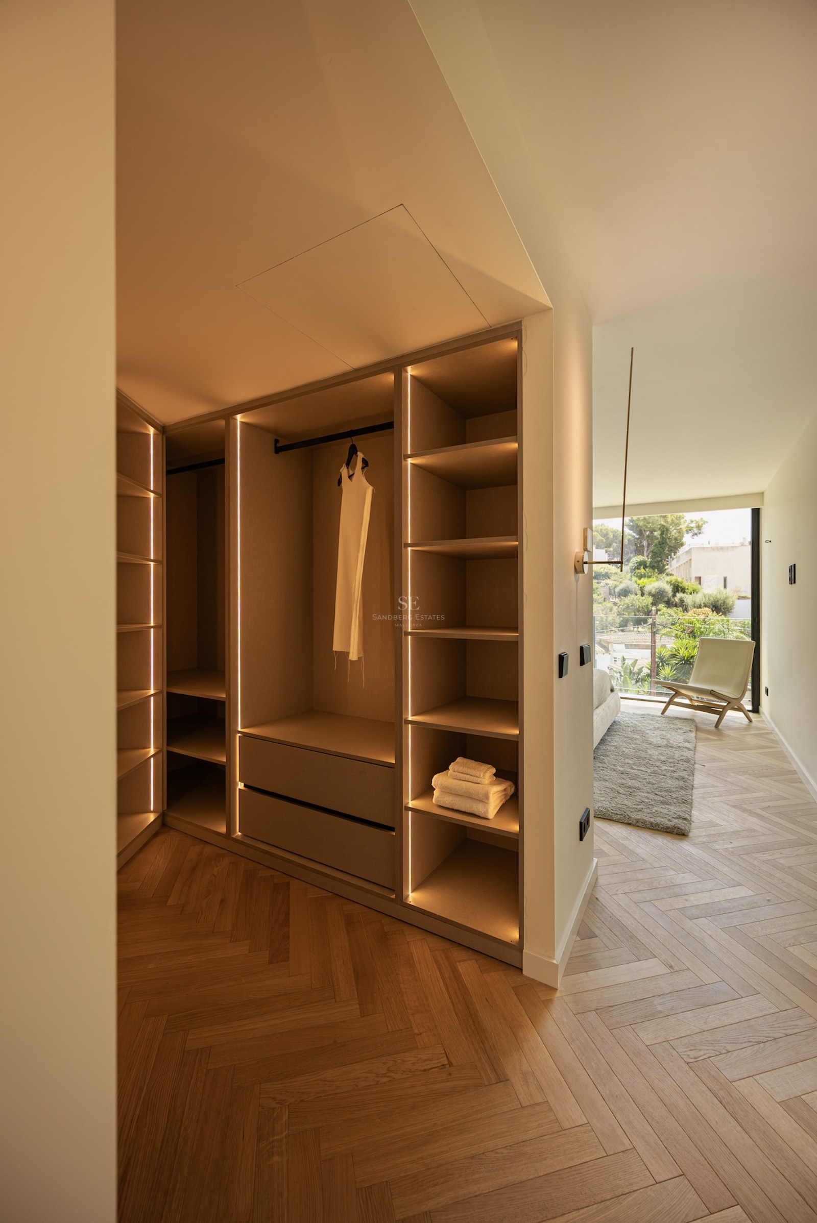 A modern walk-in closet with light wood shelving, integrated vertical LED strips, and herringbone parquet flooring.