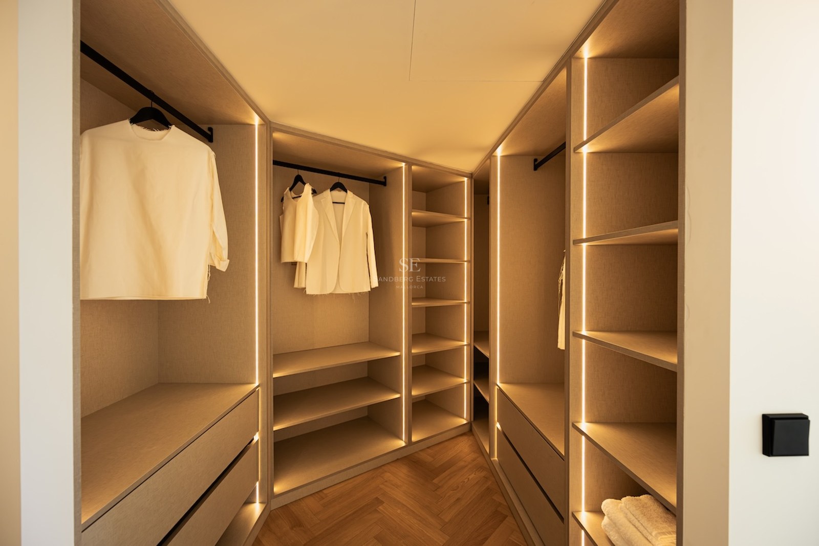 Dressing spacieux avec étagères en bois clair, éclairage LED intégré et parquet en chevrons.