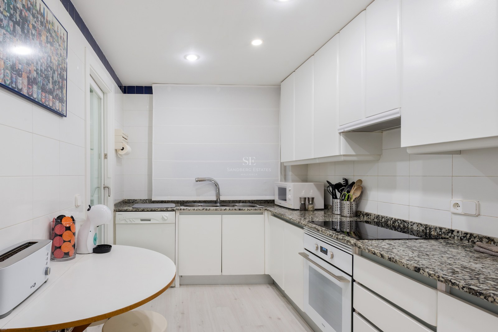 Cuisine moderne blanche avec plans de travail en granit, appareils intégrés et un petit coin petit-déjeuner.