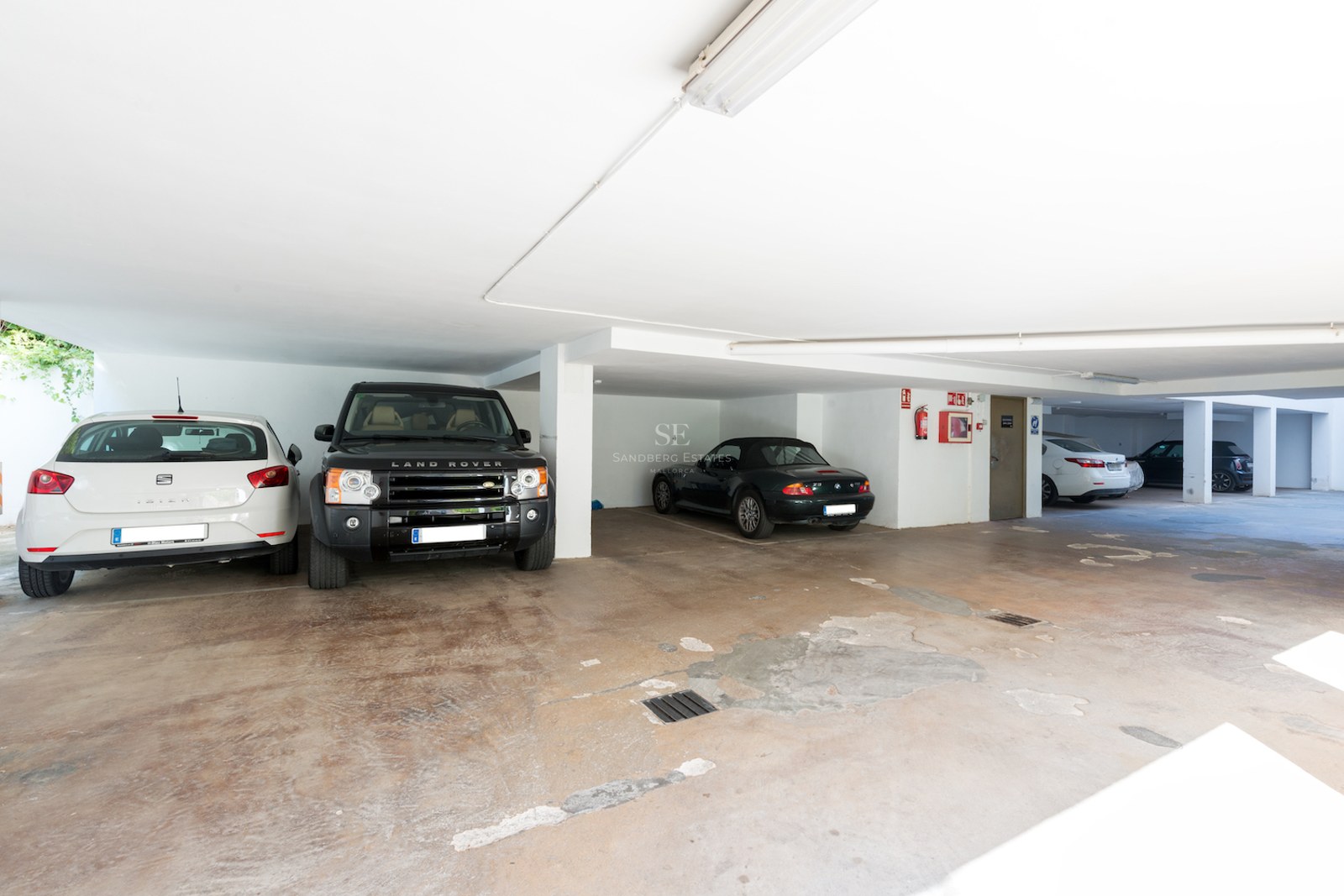 Bright underground parking garage with luxury vehicles parked in spacious designated bays.