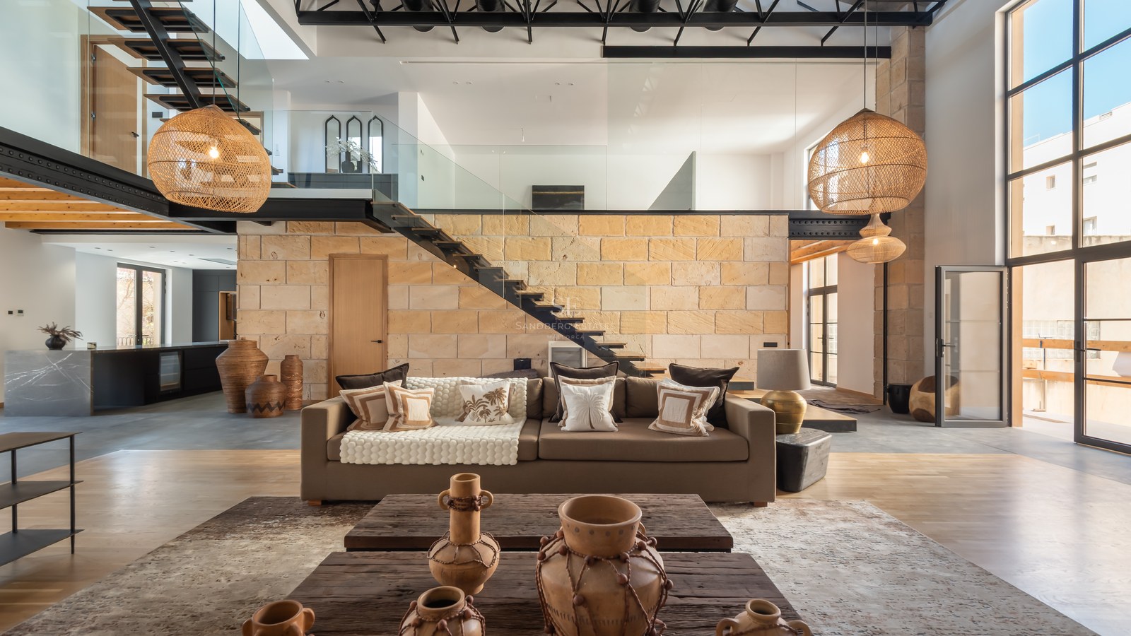 Modern living room featuring a stone wall, floating staircase, large wicker lamps, and a comfortable brown sofa.