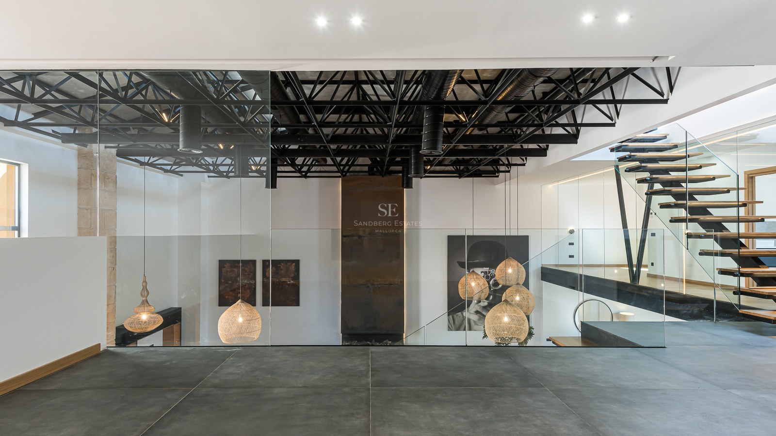 Modern interior featuring black steel ceiling trusses, glass railings, floating wood stairs, and designer pendant lamps.