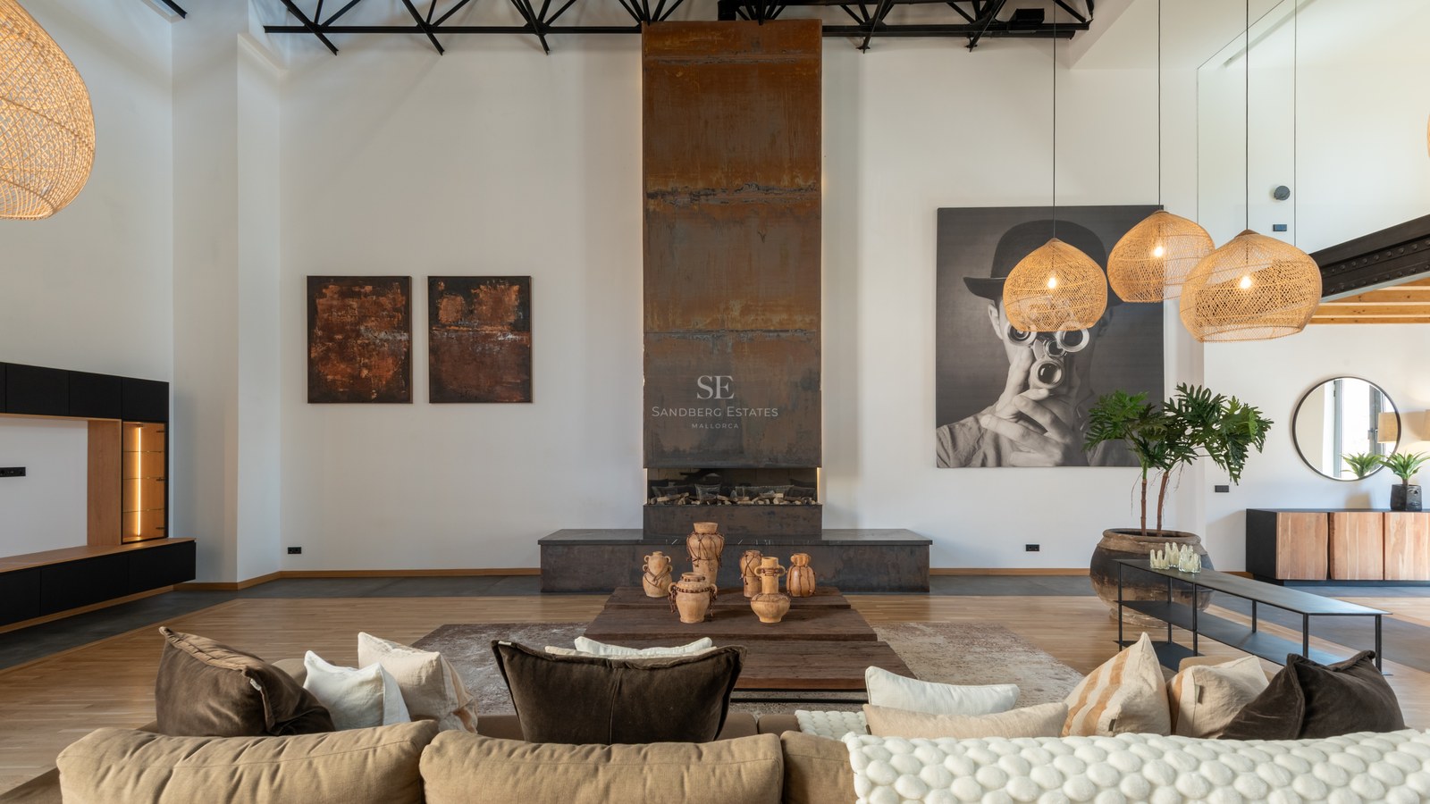 Spacious living room with a tall weathered steel fireplace, beige sofa, and woven pendant lamps in an industrial loft.