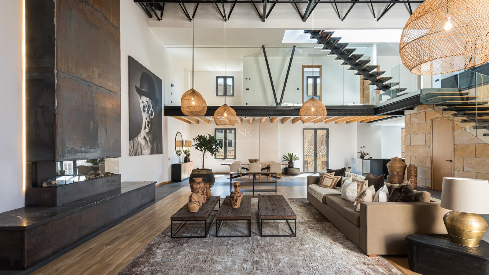 Spacious modern living room with a steel fireplace, high ceilings, floating staircase, and designer decor.