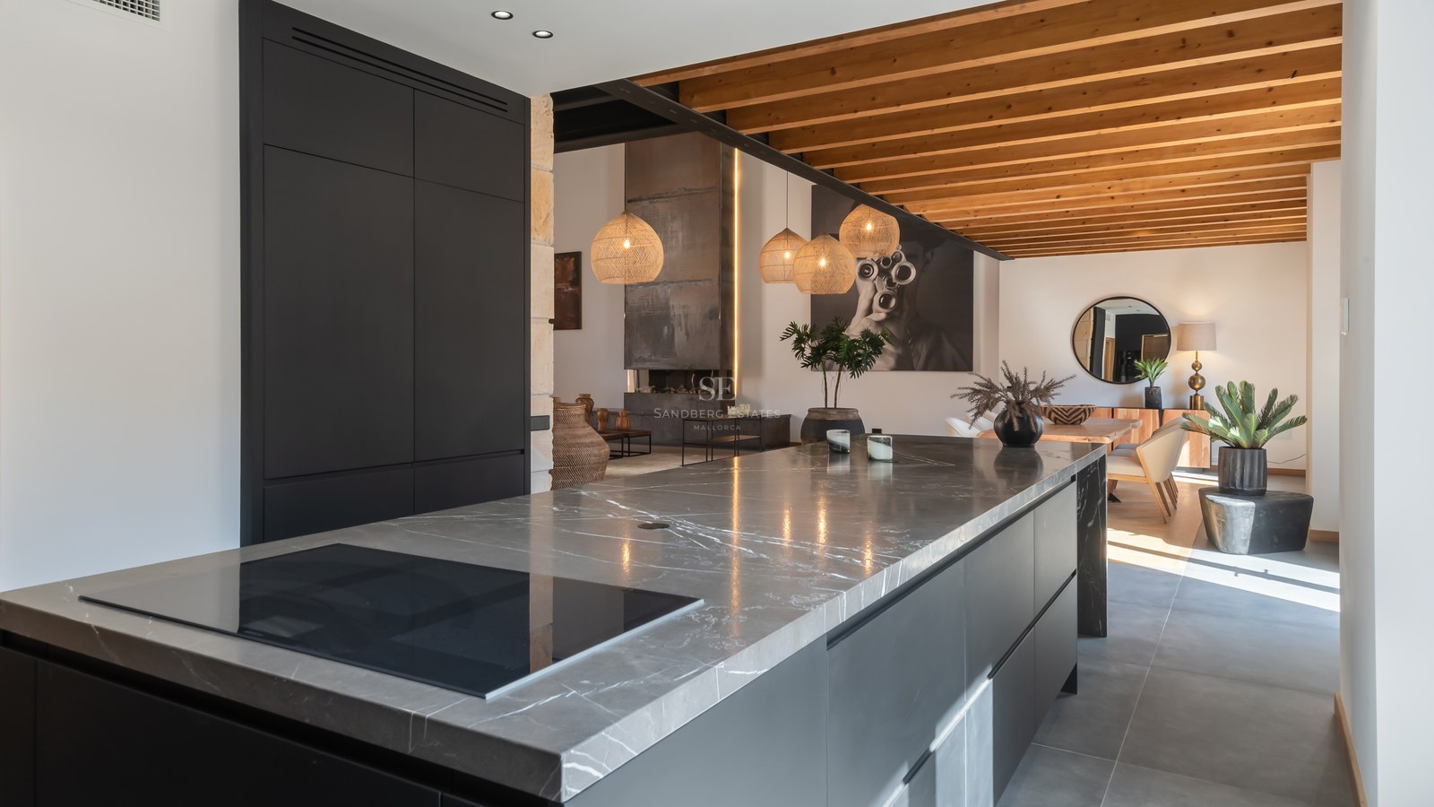 Modern kitchen featuring a large grey marble island, matte black cabinets, and exposed wooden ceiling beams.