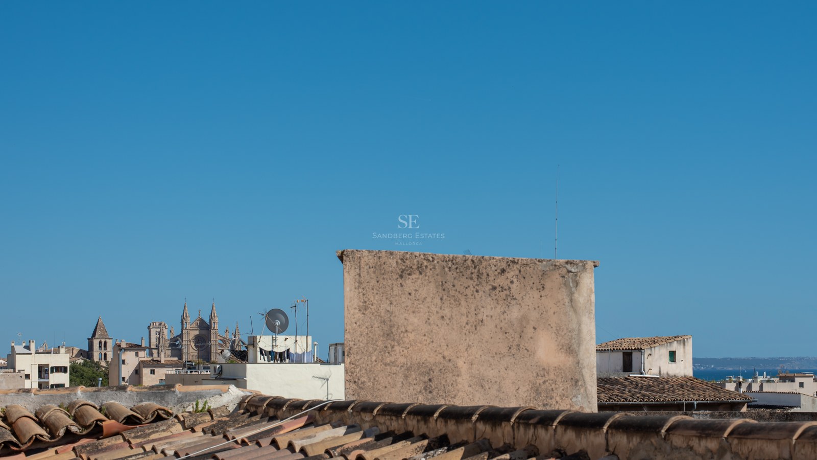View from a tiled rooftop overlooking a historic Mediterranean city with a large Gothic cathedral under a clear blue sky.