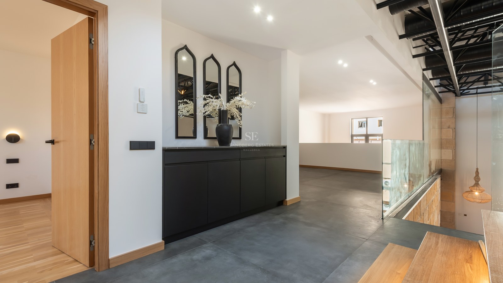 Modern hallway with black cabinetry, arched mirrors, grey tile floors, and a glass railing overlooking the lower floor.