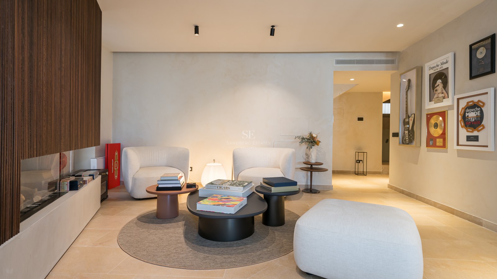 Modern living space with two white armchairs, coffee tables, a wood-slatted fireplace, and music-themed wall art.