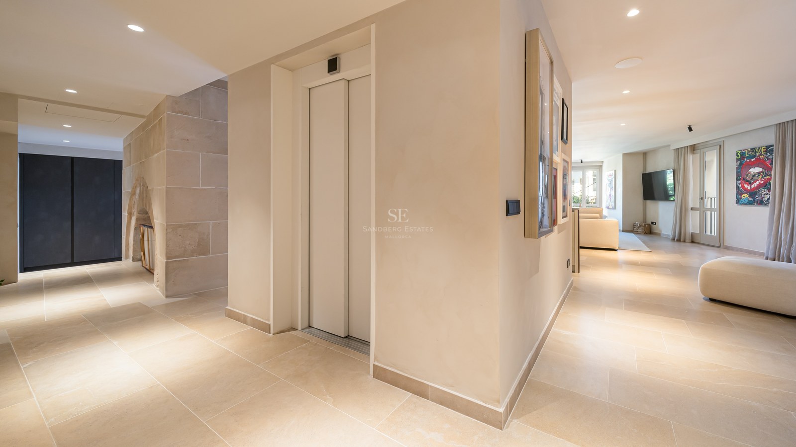 Spacious modern home entrance featuring a private elevator, beige stone floors, and a view into a bright living room.