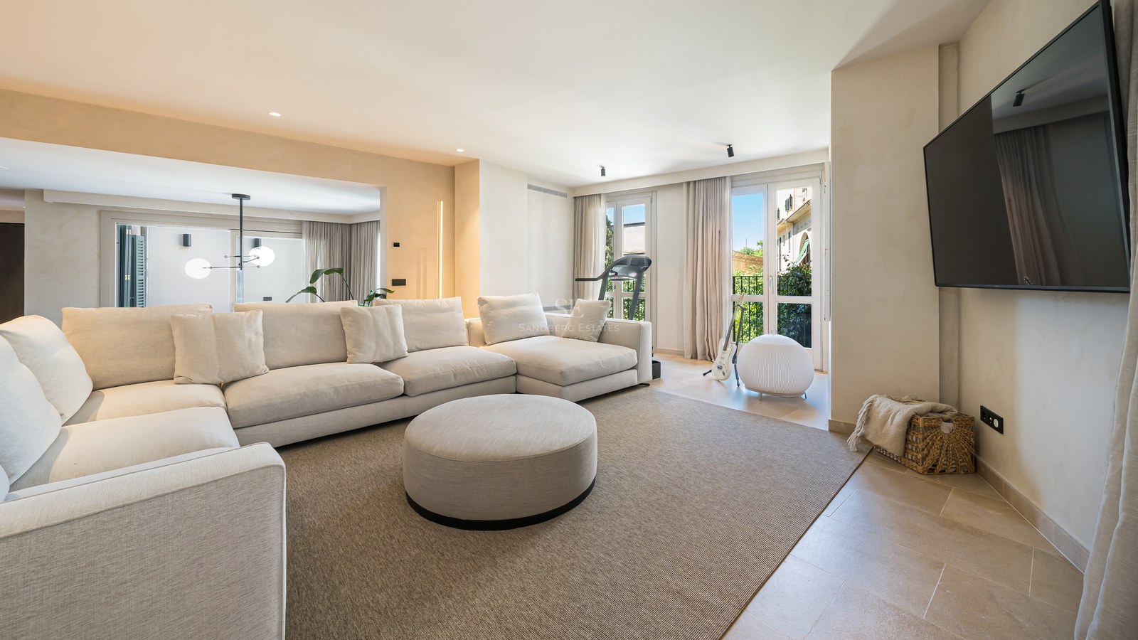 Bright living room featuring a large cream sectional sofa, beige rug, and wall-mounted flat-screen TV.