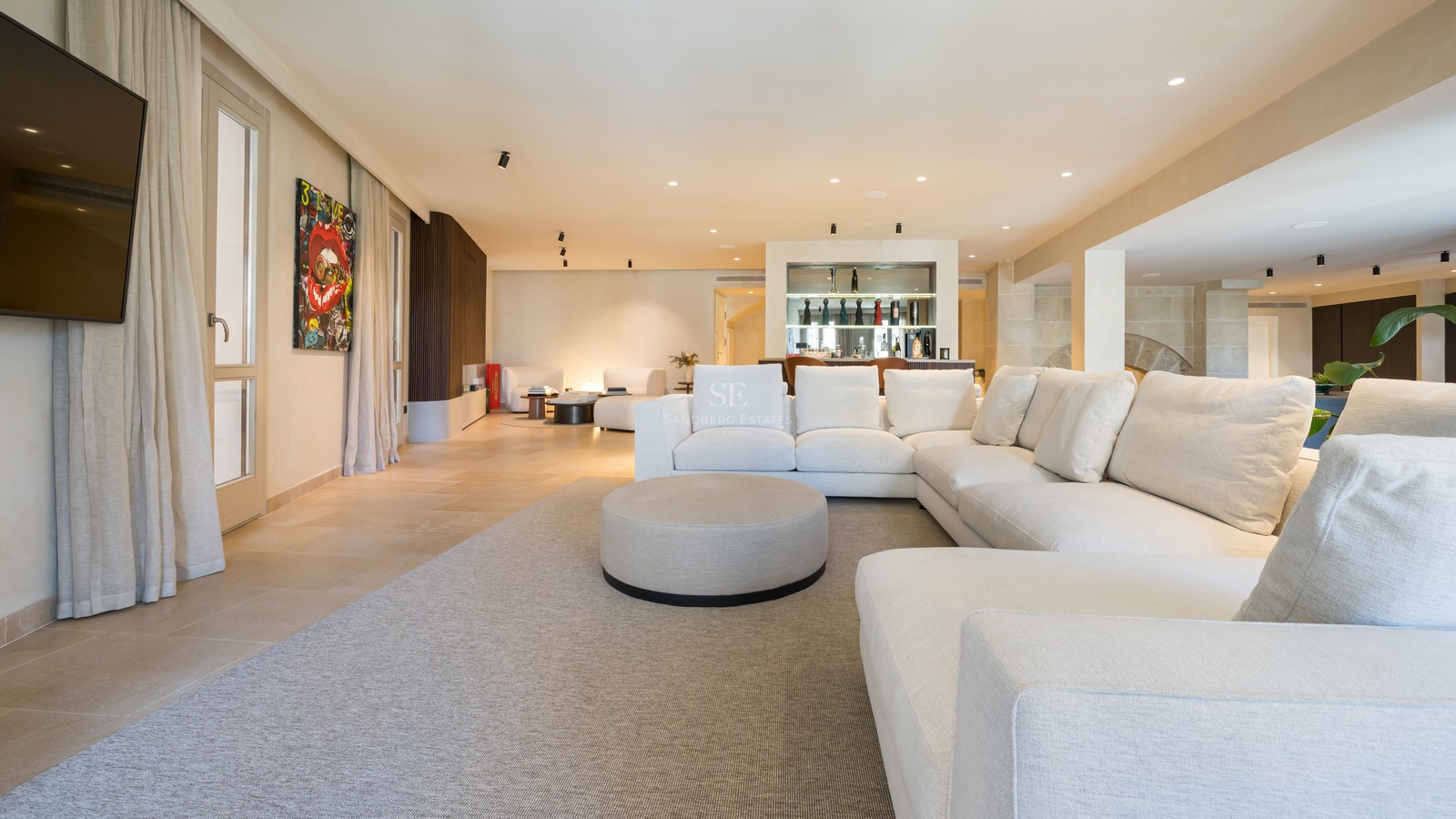 Large white sectional sofa in a spacious, modern living room with stone floors and a built-in bar area.