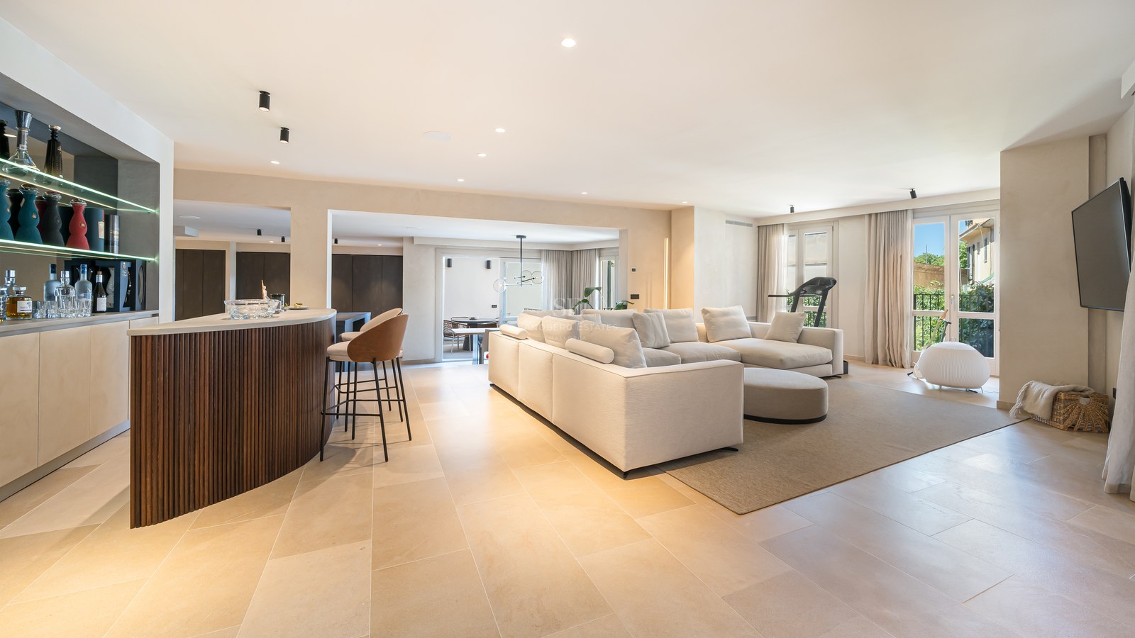Spacious modern living room with a large white sofa, wooden bar counter, and natural stone flooring.