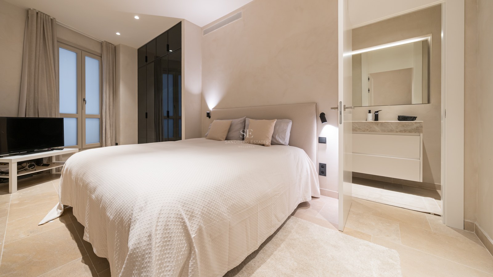 A contemporary bedroom featuring a large bed, dark glass wardrobes, and an open door leading to a modern bathroom.