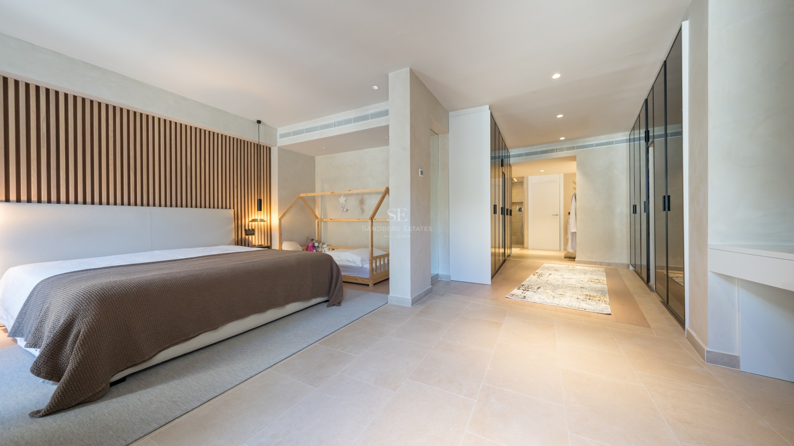 Modern bedroom featuring a wood slat wall, large bed, toddler area, and sleek glass-fronted wardrobes.