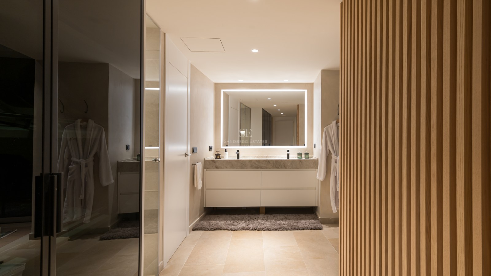 Modern bathroom featuring a marble double vanity, large backlit LED mirror, and vertical wood slat wall.