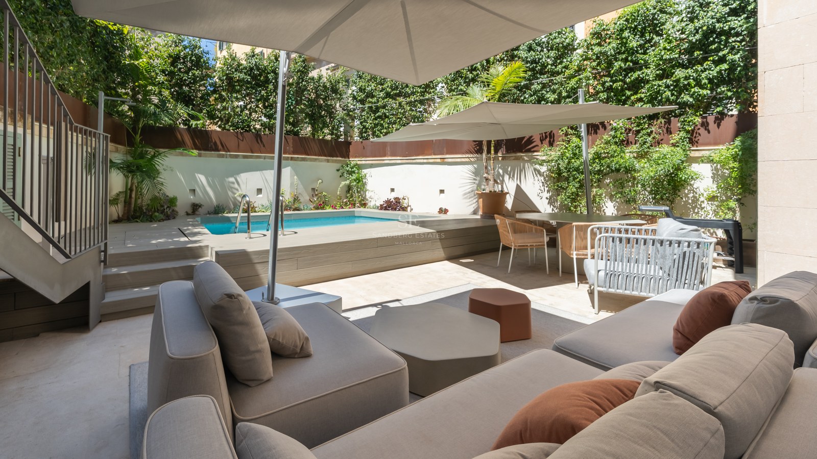 Sun-drenched terrace featuring a private pool, modern grey sofas with terracotta pillows, and large white umbrellas.