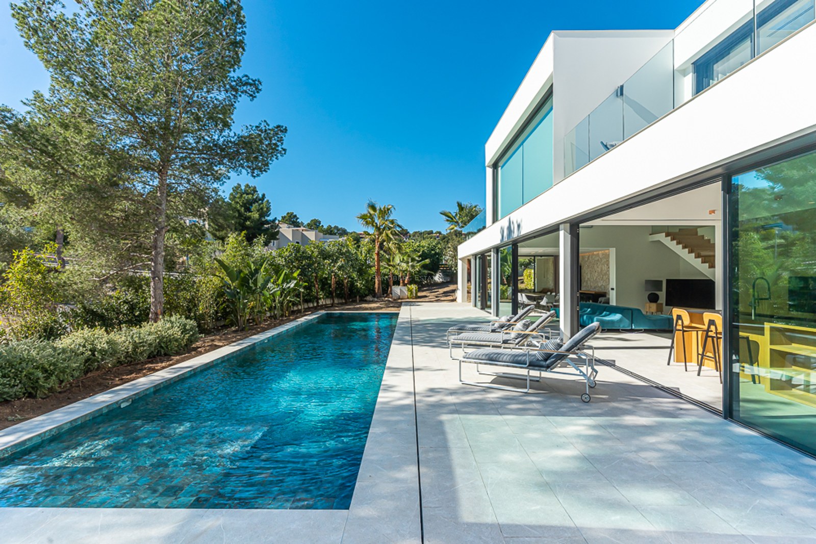 Utsikt över en modern pool med solstolar och parasoller. Ren och minimalistisk arkitektur, omgiven av grönska.