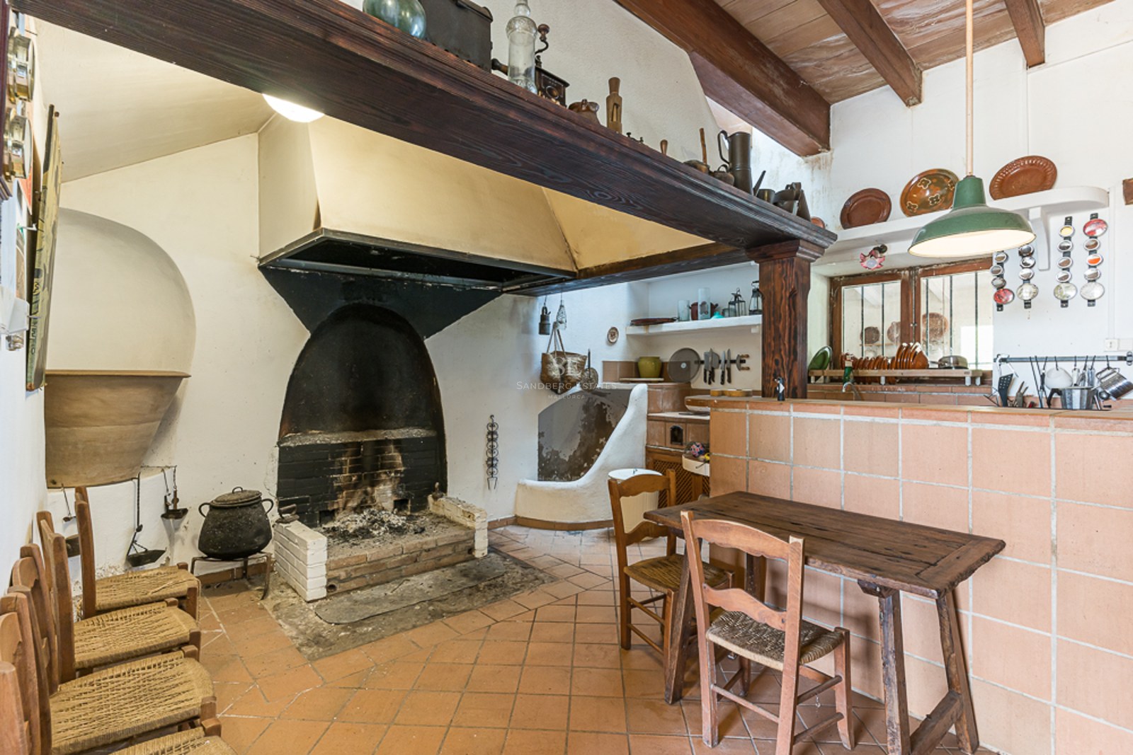 Rustic kitchen with a large open hearth fireplace, terracotta tile floor, and traditional wooden furniture.
