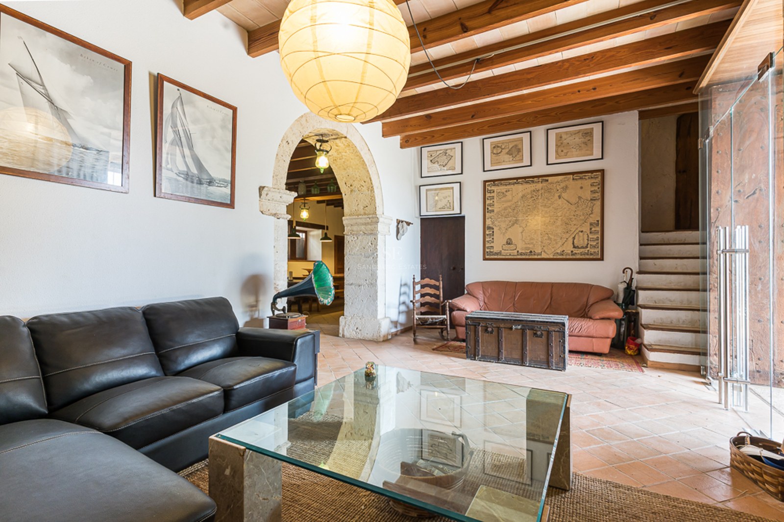 Living room with leather sofas, glass coffee table, stone archway, wooden beams, and terracotta tiles.