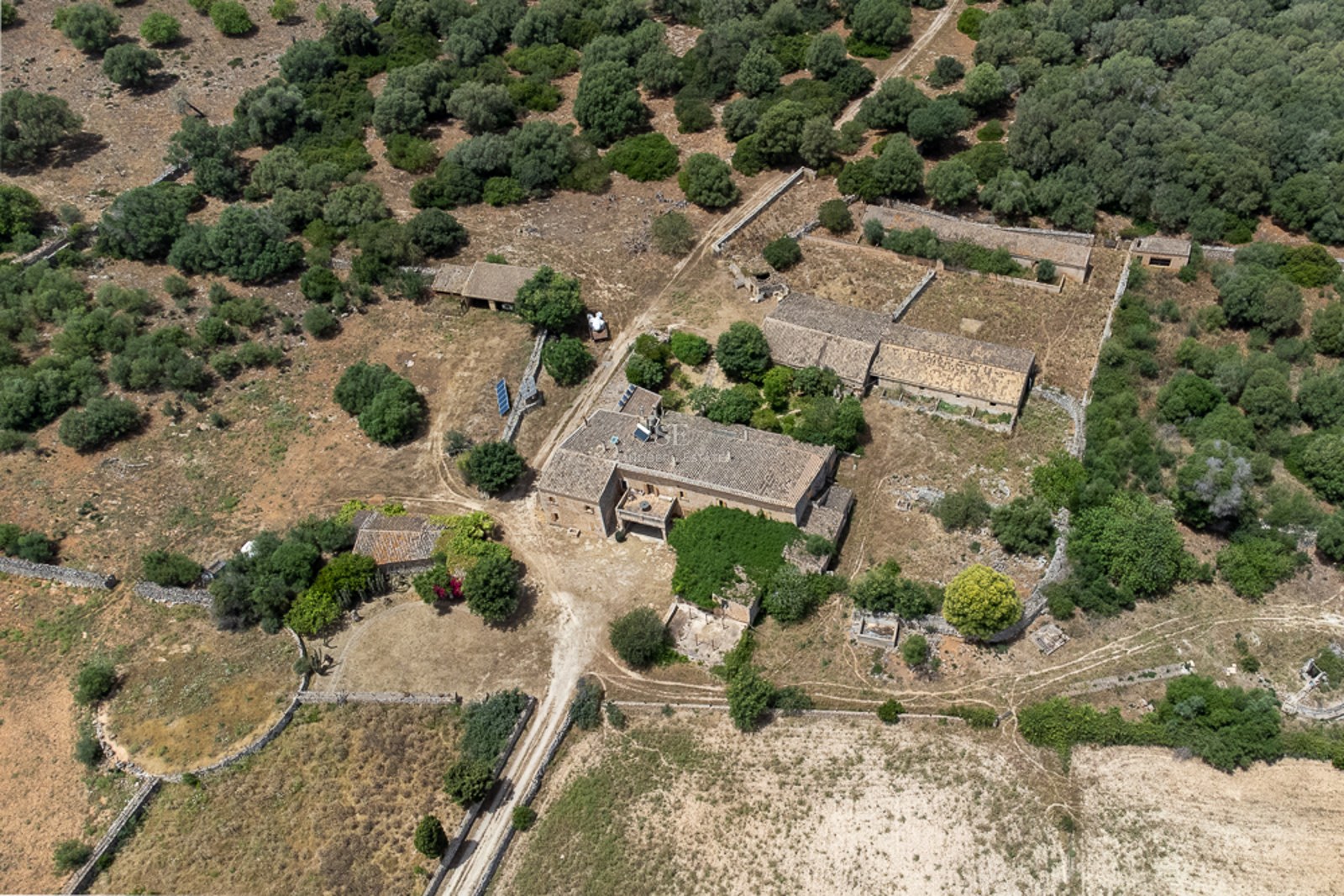 Aerial view of a large rural compound with traditional stone buildings surrounded by Mediterranean vegetation.
