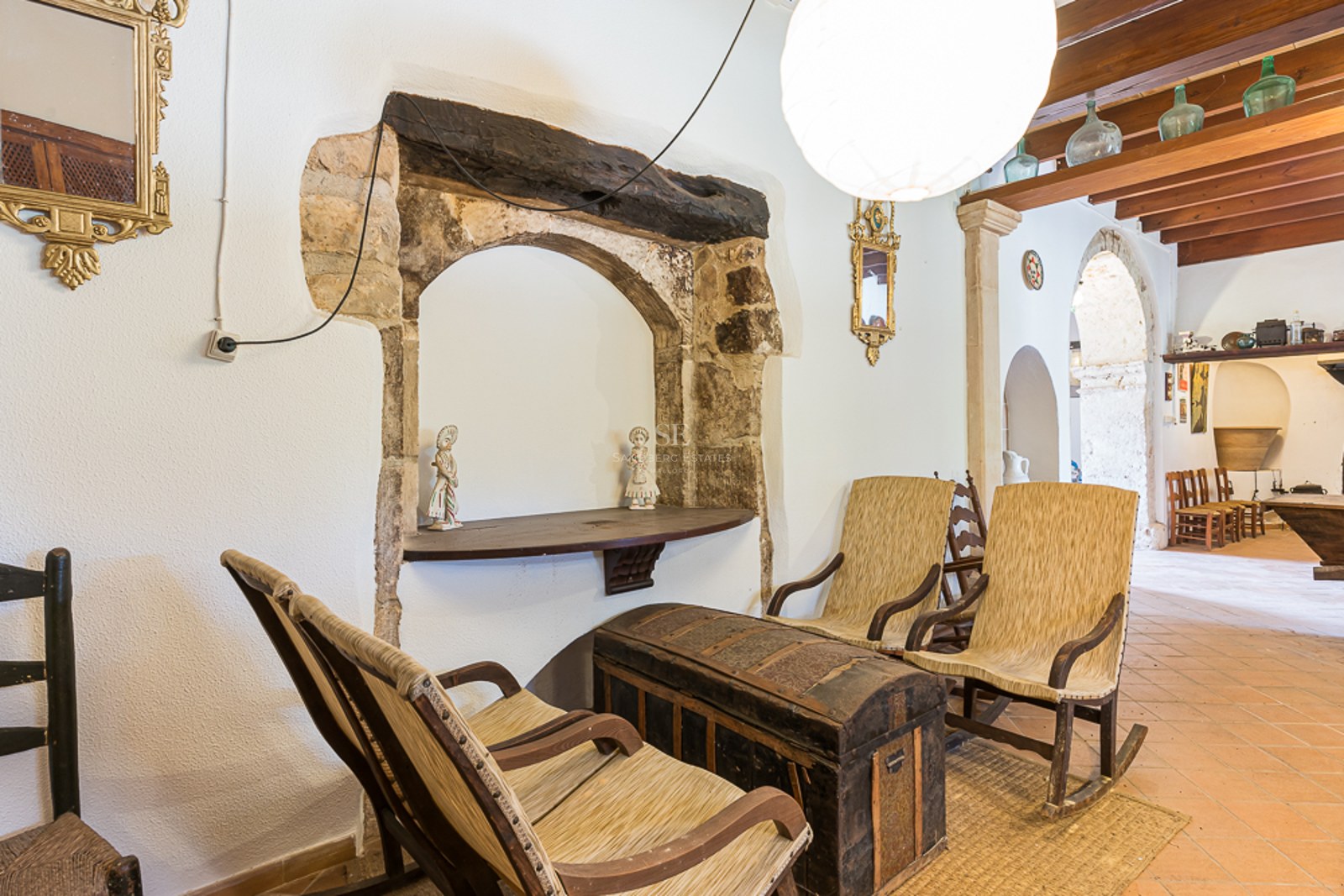 Interior with rustic rocking chairs, an antique chest, terracotta floors, and a historic stone archway.