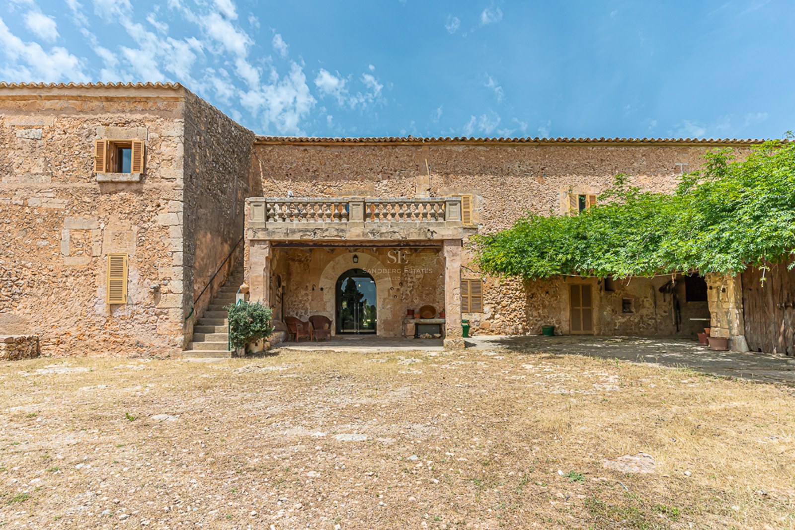 Exterior view of a rustic stone house with wooden shutters and a balcony under a bright blue sky.