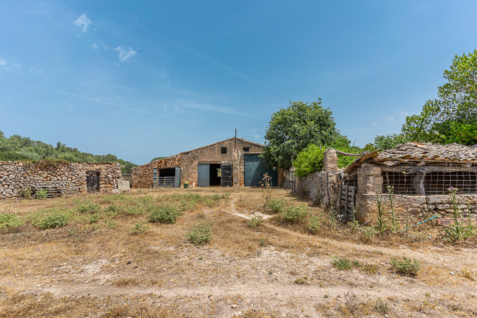 View of traditional stone buildings and dry-stone walls in a rural countryside setting under a clear blue sky.