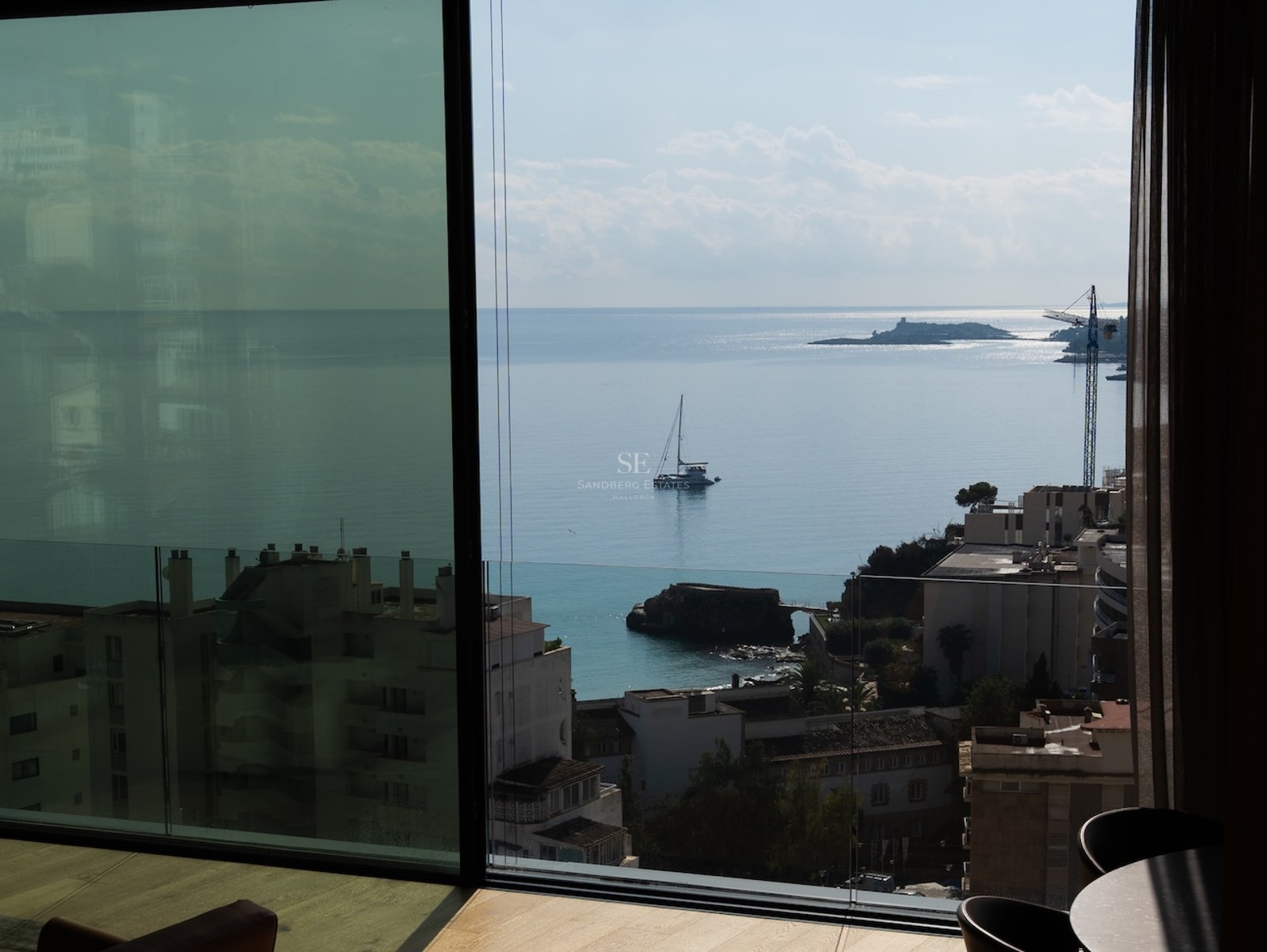 View from a modern interior through floor-to-ceiling glass looking out at the azure sea with a boat and coastline.
