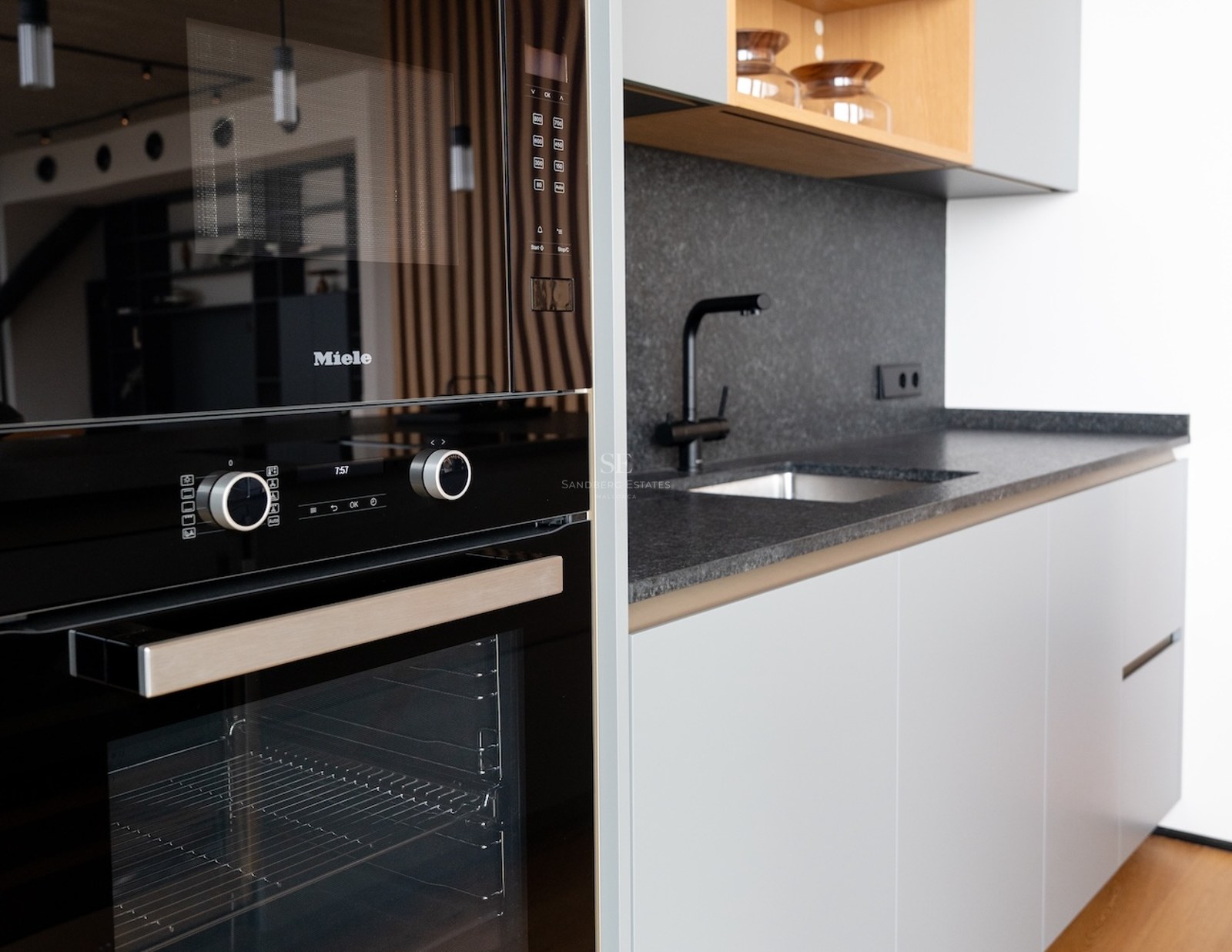 Nahaufnahme einer modernen Küche mit schwarzem Miele-Backofen, Granit-Arbeitsplatten und hellgrauen Schränken.