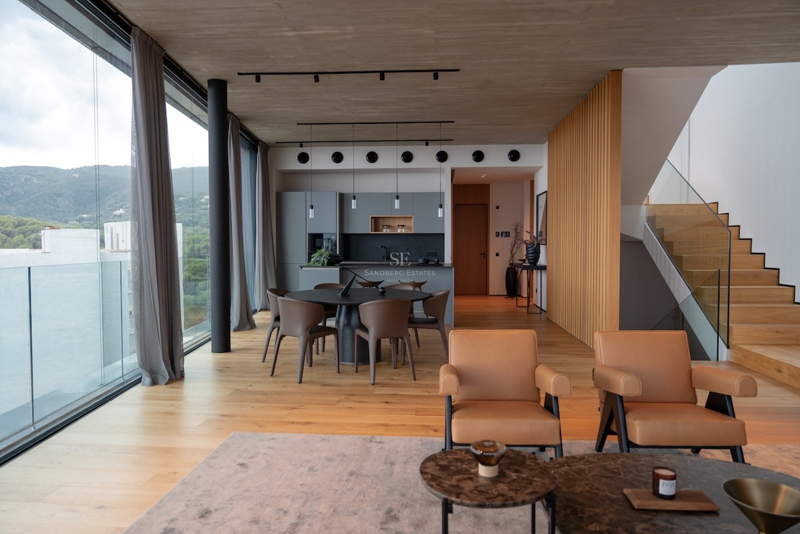 Bright open-concept living room with floor-to-ceiling windows, oak floors, concrete ceiling, and mountain views.