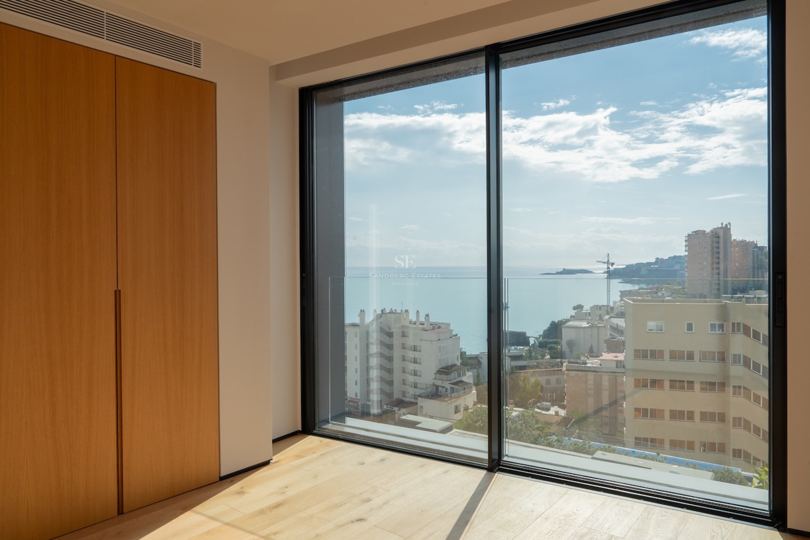 Innenansicht eines Schlafzimmers mit Eichenparkett und Einbauschränken vor einem großen Fenster mit Blick auf das Meer.