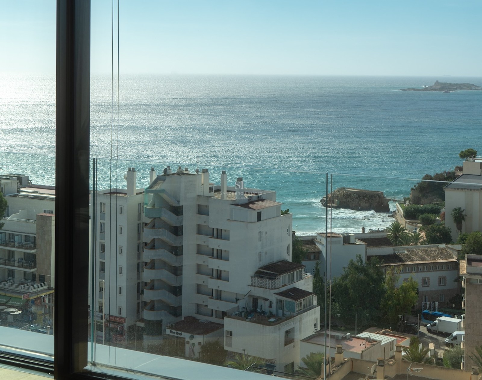 View of the Mediterranean Sea from a modern balcony with glass railings and coastal buildings in the foreground.