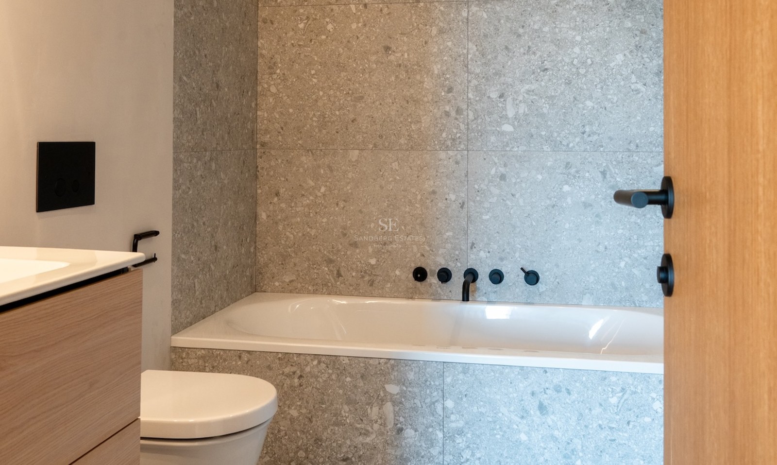 Zeitgenössisches Badezimmer mit grauen Steinfliesen, weißer Badewanne und mattschwarzen Wandarmaturen.