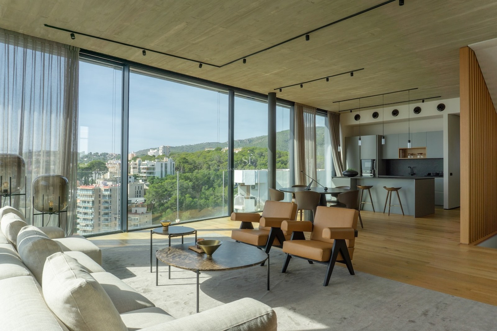 Modern open-plan living room with floor-to-ceiling windows overlooking a Mediterranean city and green hills.