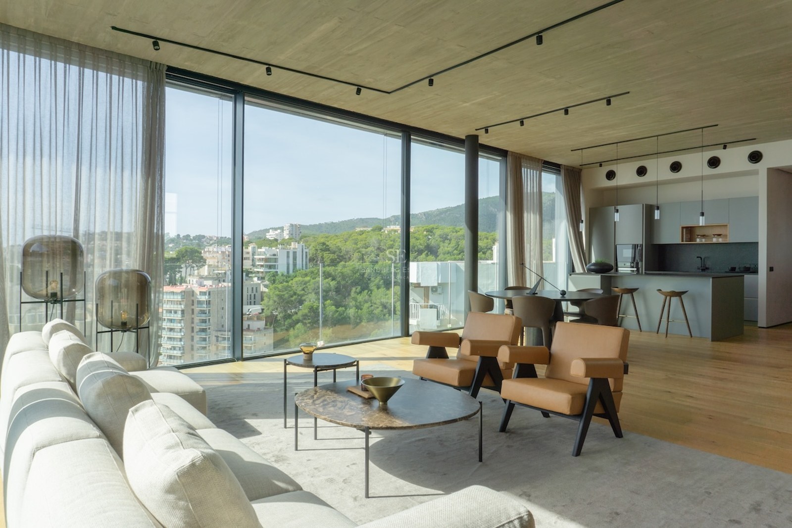 Heller Wohnraum mit bodentiefen Fenstern, Blick auf Stadt und Natur, großes graues Sofa und Designmöbel.