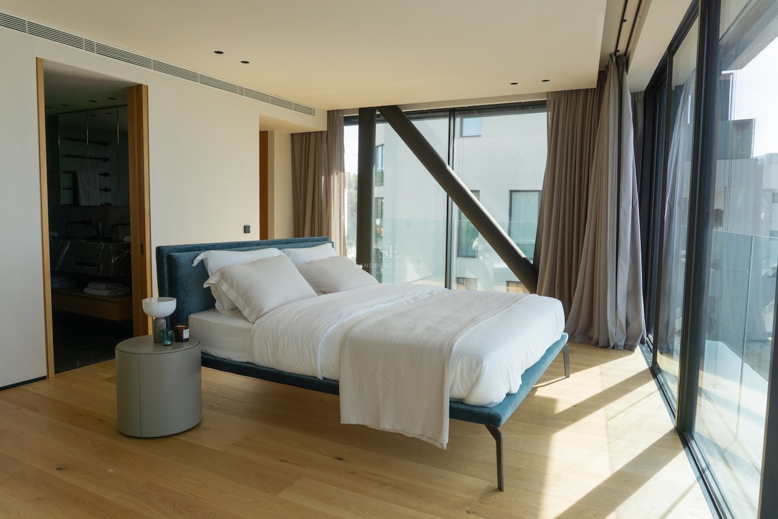 Contemporary bedroom featuring a blue fabric bed, oak flooring, and large glass walls with views.