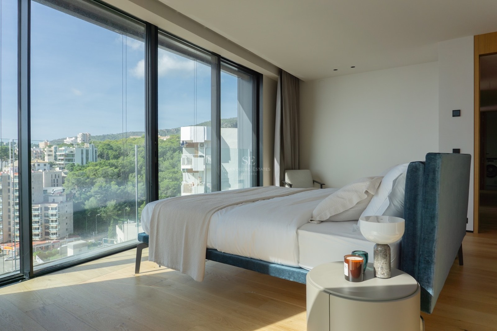 Zeitgenössisches Schlafzimmer mit bodentiefen Fenstern, Stadt- und Hügelblick, blauem Samtbett und Eichenparkett.