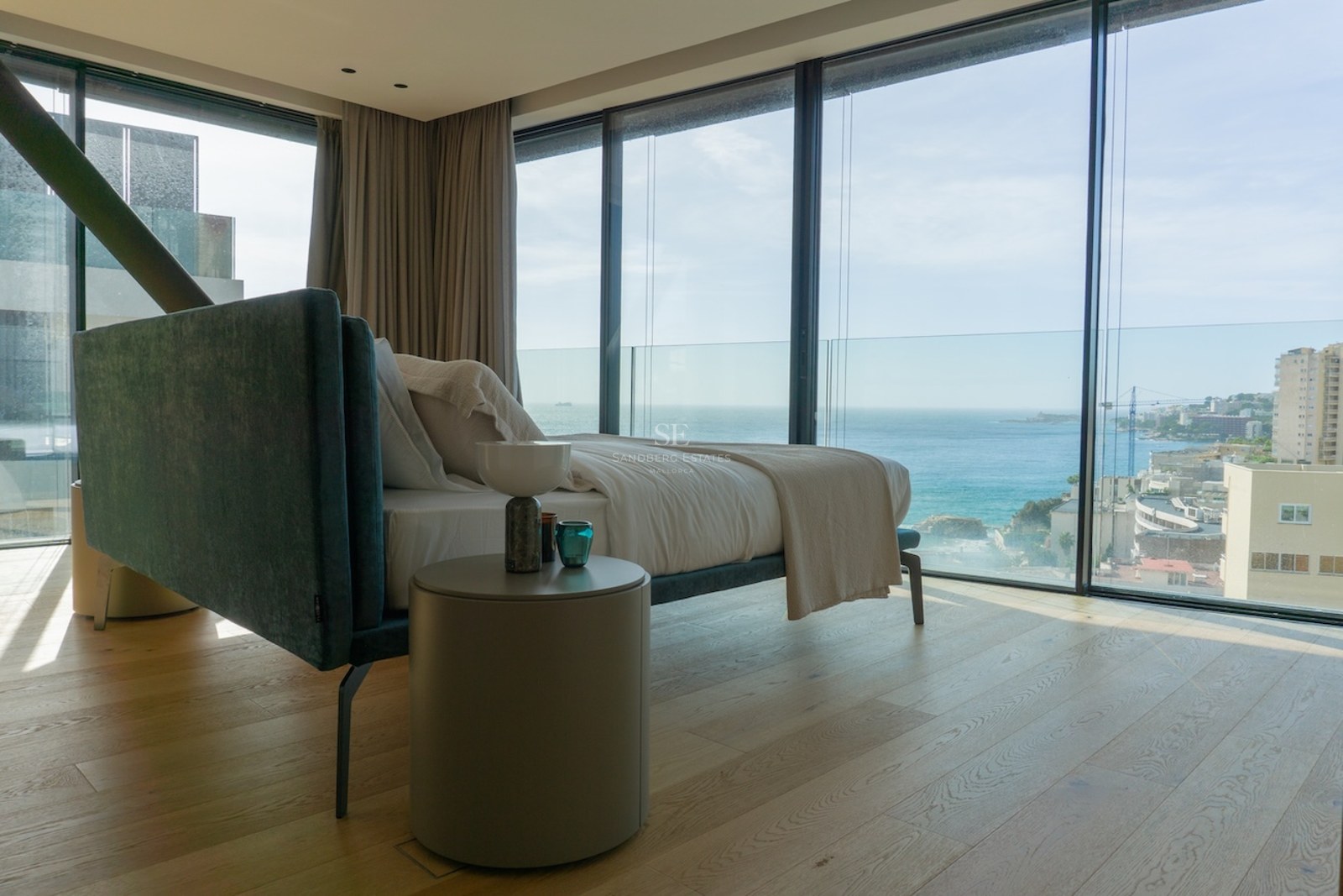 Modernes Schlafzimmer mit Eichenparkett und bodentiefen Glasfenstern mit Blick auf das Mittelmeer und die Küste.