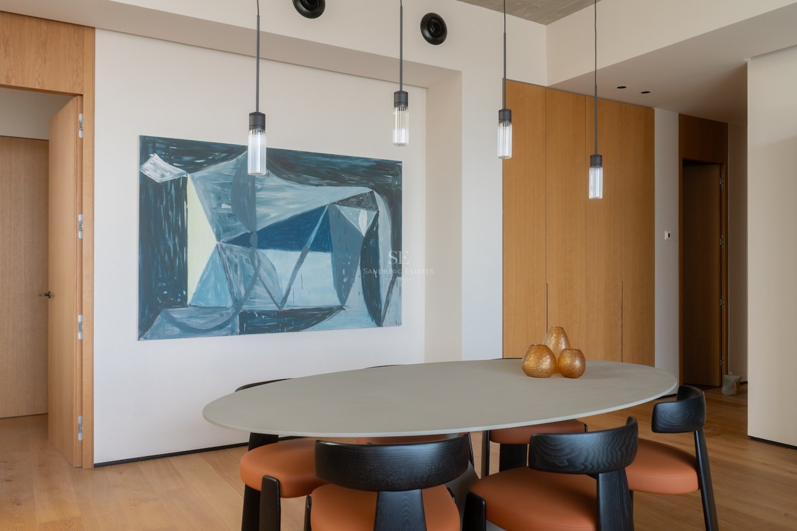 Modernes Esszimmer mit ovalem grauem Tisch, orangefarbenen Lederstühlen und abstrakter blauer Wandkunst.