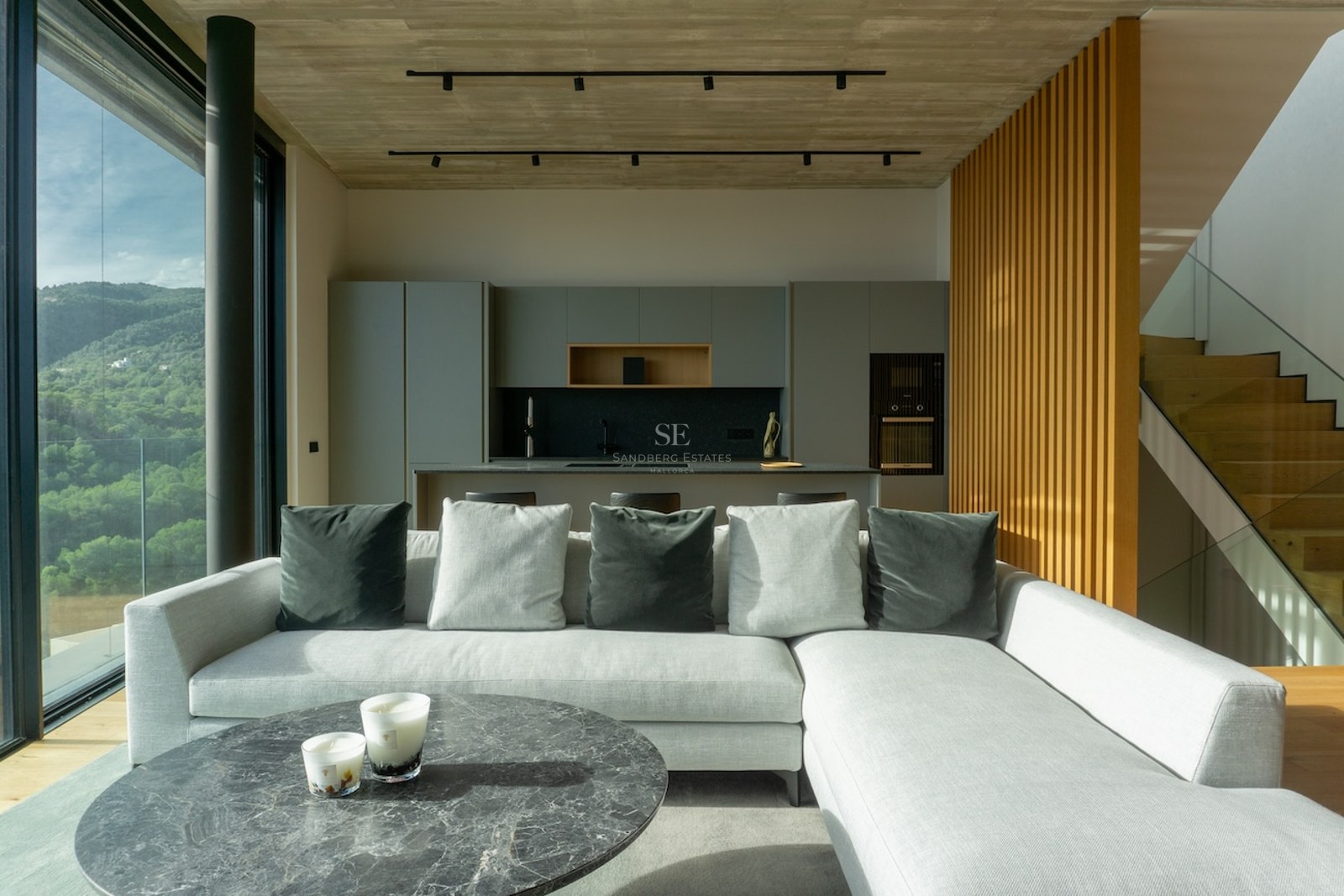 Modernes Wohnzimmer mit grauem Sofa, Marmortisch und bodentiefen Fenstern mit Blick auf grüne Hügel.