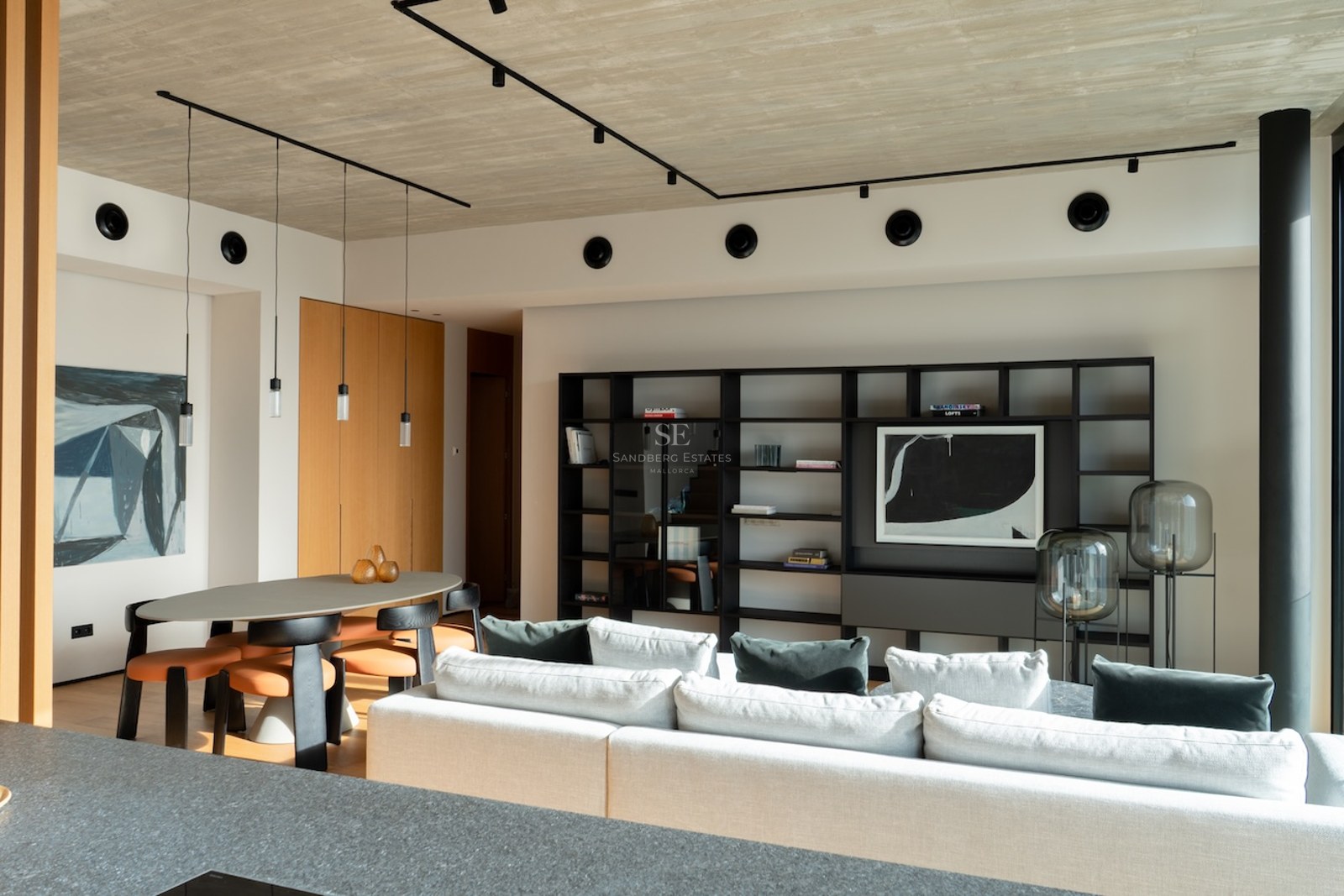 Modernes Wohnzimmer mit Beton-Decke, weißem Sofa, Essbereich und schwarzem Designer-Regal.