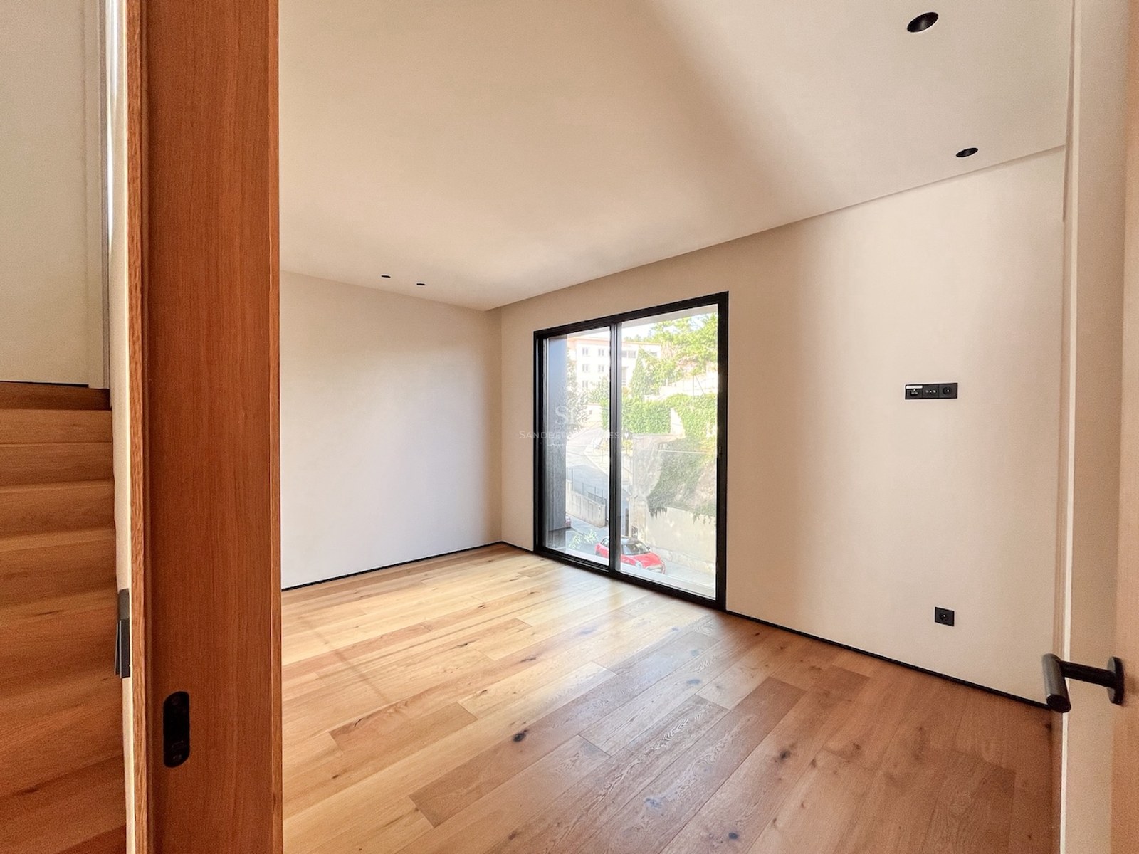 Helles Schlafzimmer mit Eichenholzboden, cremefarbenen Wänden und großem Fenster mit schwarzem Rahmen.