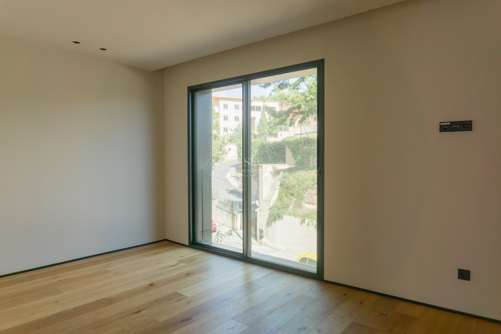 Empty modern bedroom featuring wide-plank oak floors, white walls, and a large sliding glass door.