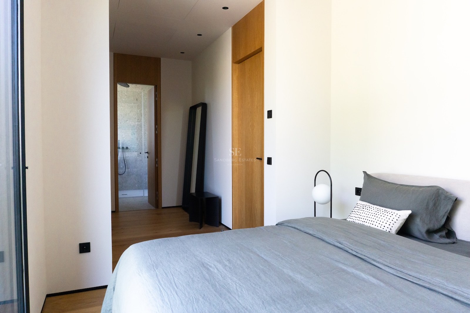 Helles minimalistisches Schlafzimmer mit Leinenbettwäsche, Eichenparkett und Blick in ein Naturstein-Bad.