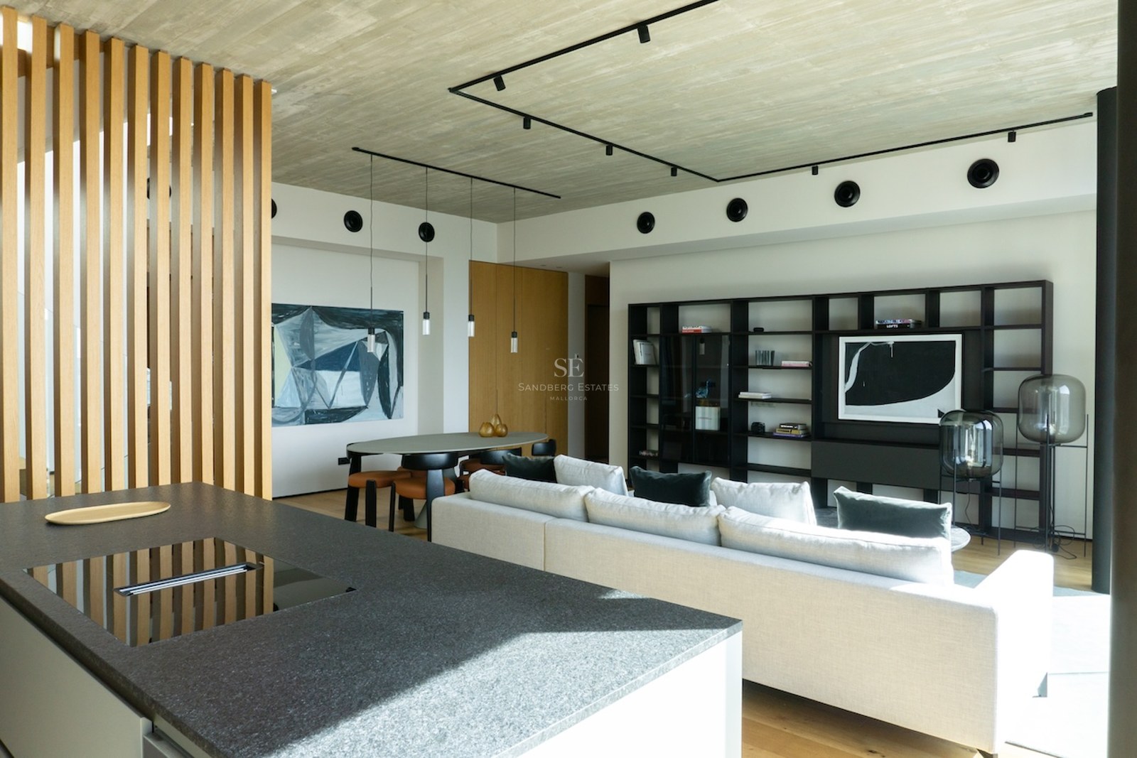Moderner offener Wohnbereich mit Kücheninsel aus Stein, weißem Sofa und Sichtbetondecke.