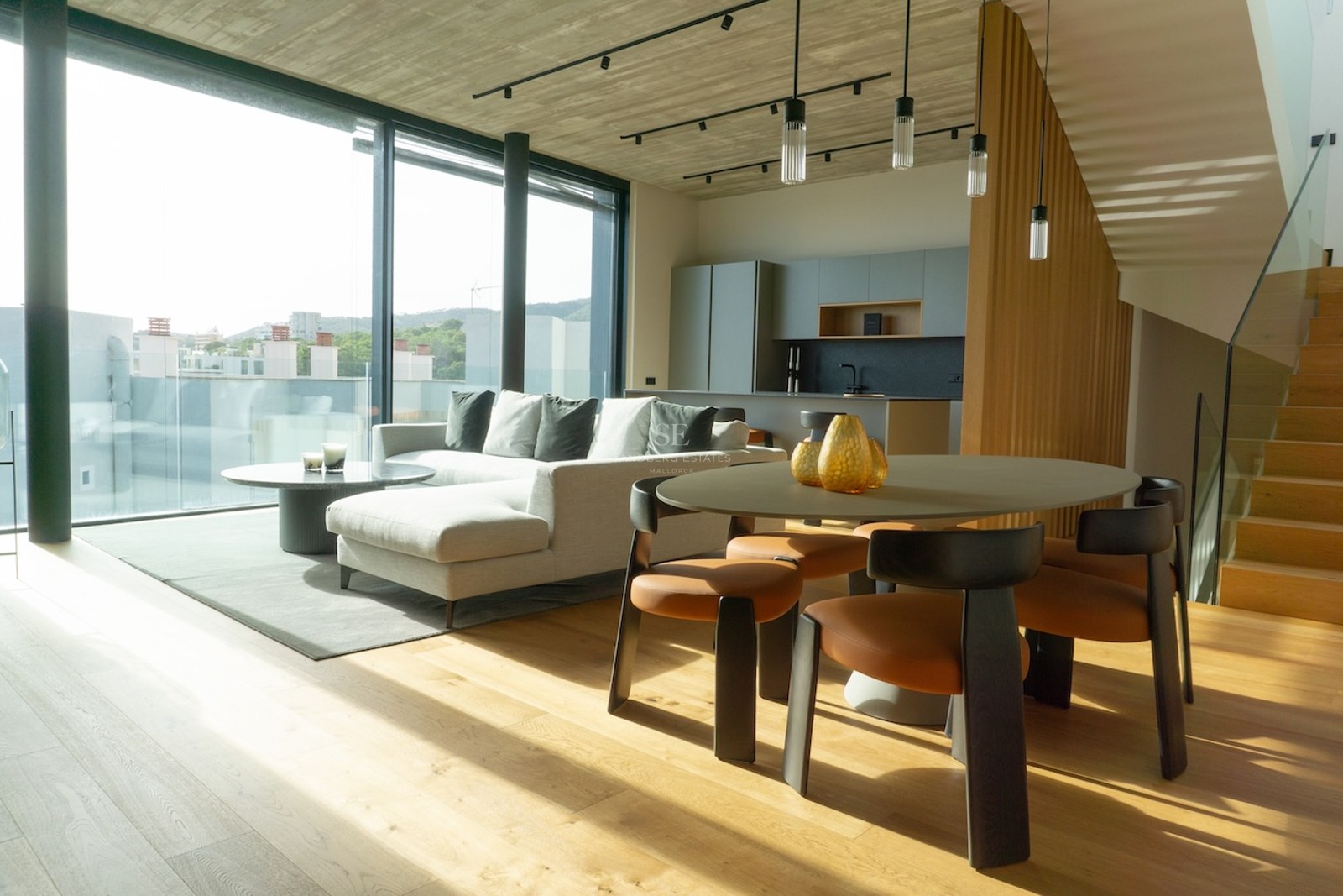 Heller, offener Wohnraum mit bodentiefen Fenstern, grauem Sofa, Holzesstisch und Sichtbetondecke.